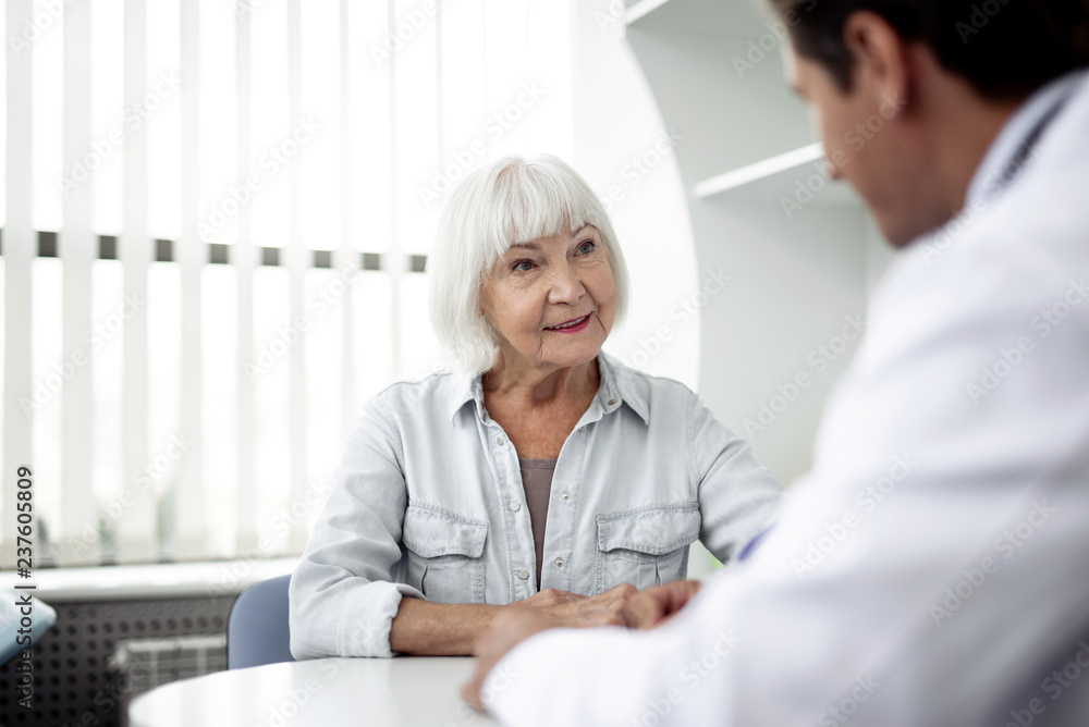 Fototapeta premium Calm elderly lady sitting in front of her practitioner and feeling interested while talking to him and smiling