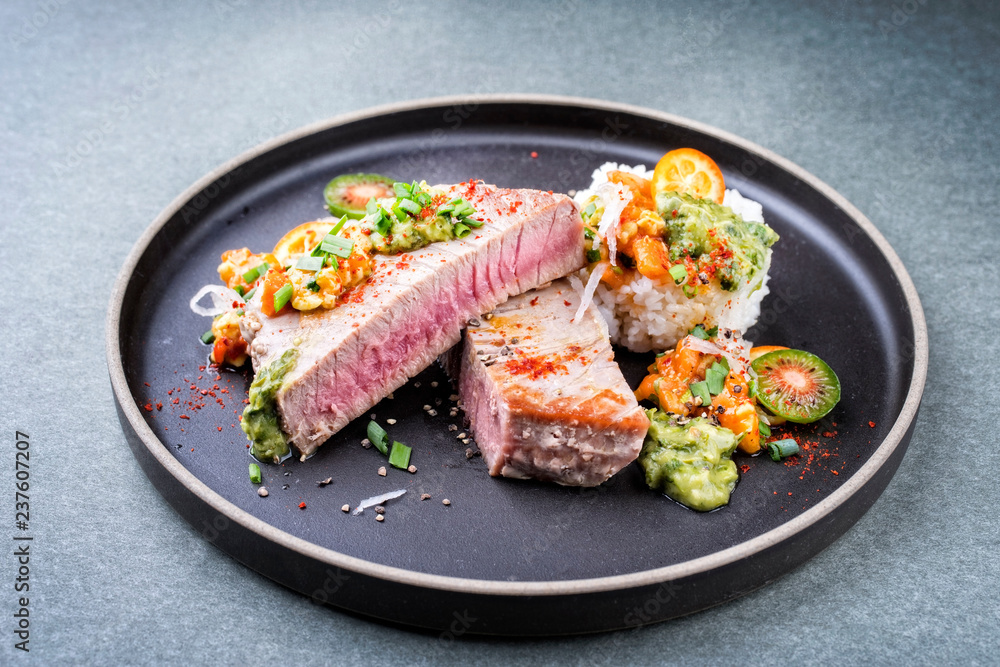 Traditional exotically tuna fish fillet with mango salsa and rice as closeup on a modern design black plate Traditional exotically tuna fish fillet with mango salsa and rice as closeup on a modern design black plate