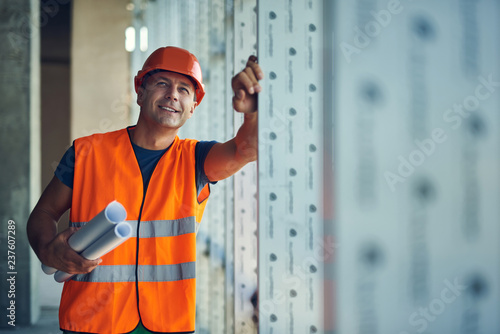 Confident professional builder holding his drawings and looking up while standing alone and smiling