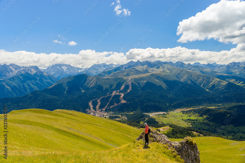 Woman on meadow in mountain of Arkhyz. The beautiful summer landscape with cloudy sky and mountain.