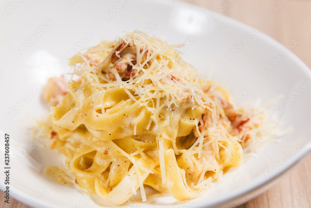 Pasta with meat and cheese in white plate on light wooden table in a restaurant