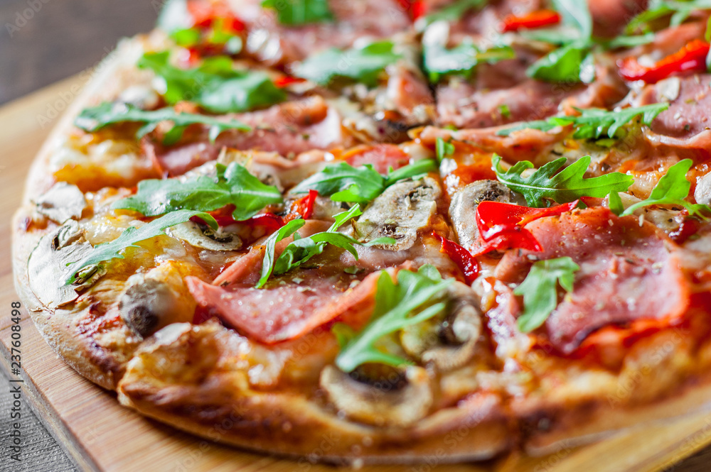 Pizza with Mozzarella cheese, mushrooms, ham, tomato sauce, salami, pepper, Spices and Fresh arugula. Italian pizza on wooden table background Pizza with Mozzarella cheese, mushrooms, ham, tomato sauce, salami, pepper, Spices and Fresh arugula. Italian pizza on wooden table background