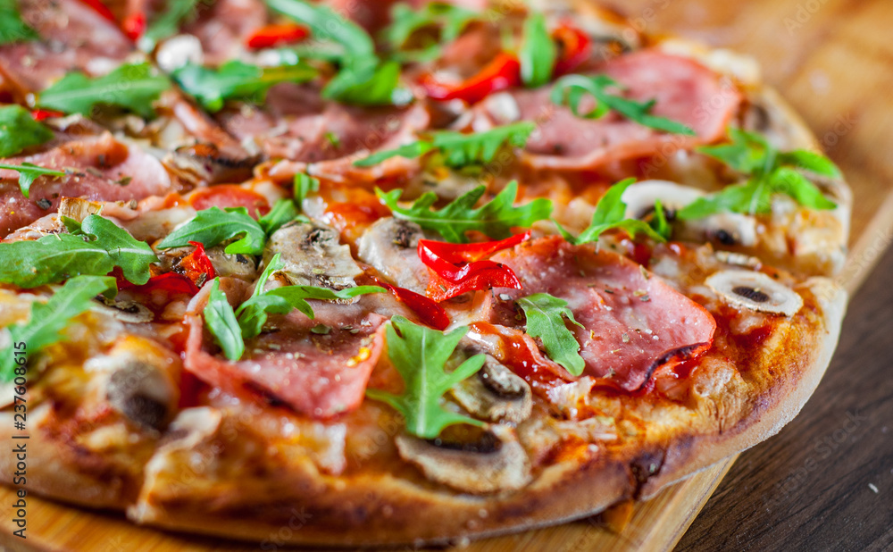 Pizza with Mozzarella cheese, mushrooms, ham, tomato sauce, salami, pepper, Spices and Fresh arugula. Italian pizza on wooden table background Pizza with Mozzarella cheese, mushrooms, ham, tomato sauce, salami, pepper, Spices and Fresh arugula. Italian pizza on wooden table background