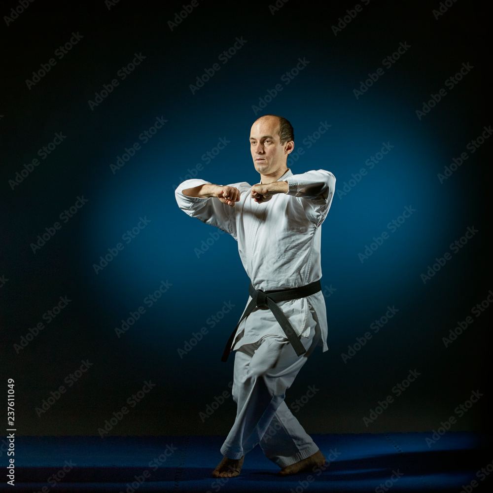 Active athlete doing formal karate exercises on a blue tatami Active athlete doing formal karate exercises on a blue tatami