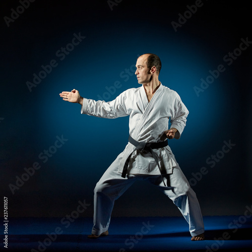 Black belt athlete trains formal karate exercises on blue tatami