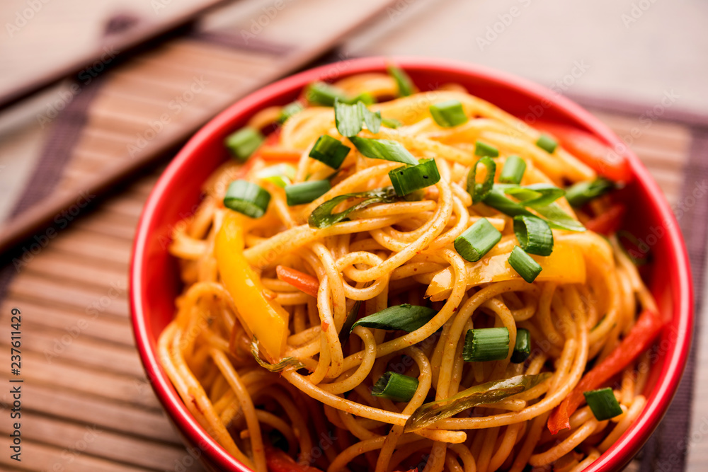 Schezwan Noodles or vegetable Hakka Noodles or chow mein is a popular Indo-Chinese recipes, served in a bowl or plate with wooden chopsticks. selective focus