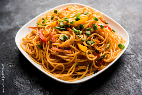 Photography Schezwan Noodles or vegetable Hakka Noodles or chow mein is a popular Indo-Chinese recipes, served in a bowl or plate with wooden chopsticks