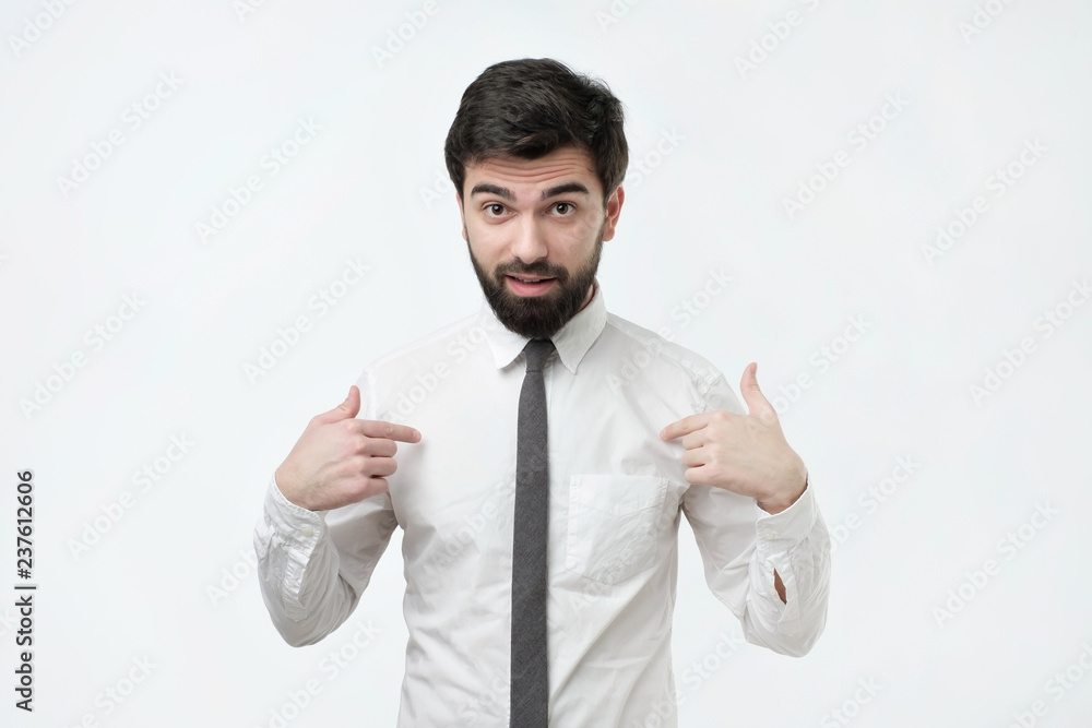 Are you talking about me. Handsome frowning spanish man with voluminous hair and beard pointing fingers at himself, having doubtful confused facial expression Are you talking about me. Handsome frowning spanish man with voluminous hair and beard pointing fingers at himself, having doubtful confused facial expression