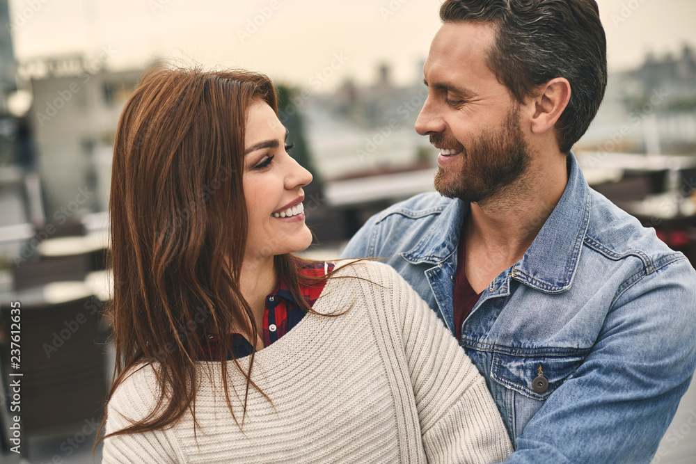 Waist up of smiling man and woman is standing on terrace and hugging Waist up of smiling man and woman is standing on terrace and hugging