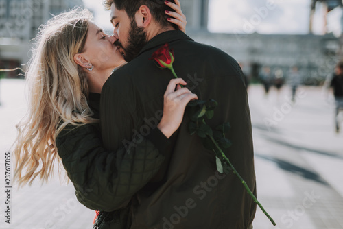 Waist up portrait of charming lady holding red rose and sharing romantic moment with her boyfriend