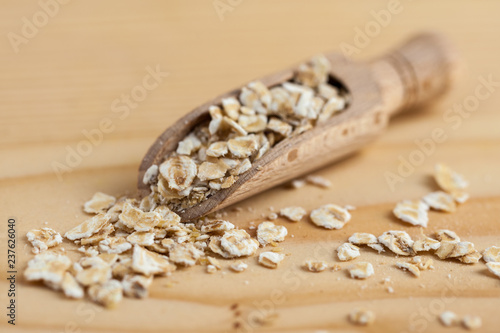 Oat flakes in a wooden bowl with a scoop on the wooden board