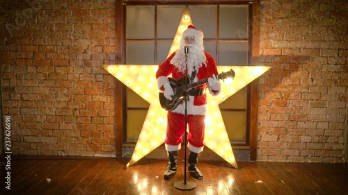 Santa Claus rock star, plays guitar, sings funny christmas songs in retro microphone