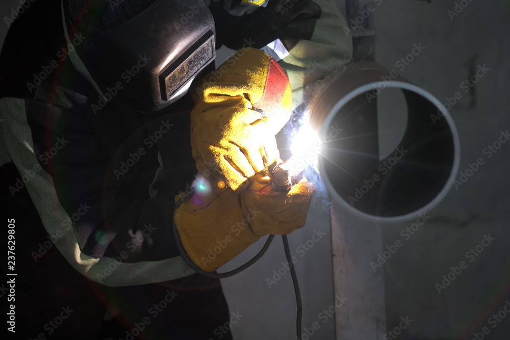 Welder uses torch to make sparks during manufacture of metal cylinder. Welder uses torch to make sparks during manufacture of metal cylinder.