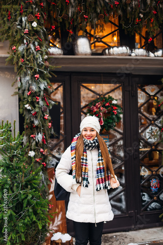 girl in winter clothes near a cafe with Christmas decorations looks in the camera lens
