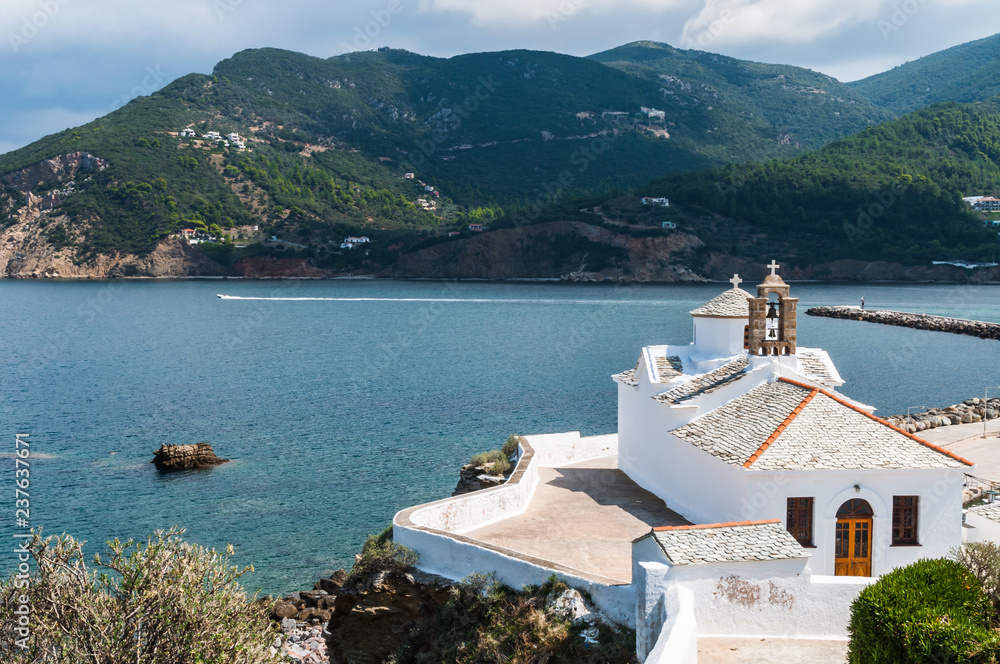 The church of the Virgin Mary (Panagitsa Tower) with stone tile on Skopelos city on backgroud of the blue sea of island bay and hills
