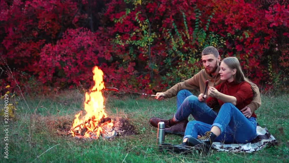 Cute romantic couple in love hugging at nice cozy picnic barbecue lunch frying food on bright flame campfire in slowmo Cute romantic couple in love hugging at nice cozy picnic barbecue lunch frying food on bright flame campfire in slowmo