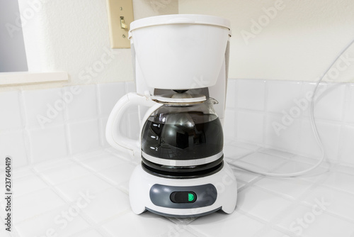 Small white coffee maker on clean white tile kitchen counter.  