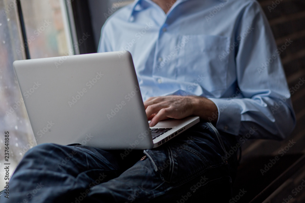 A man sits on a windowsill and works on a laptop. Beautiful man's wrist. Long fingers of a young man.