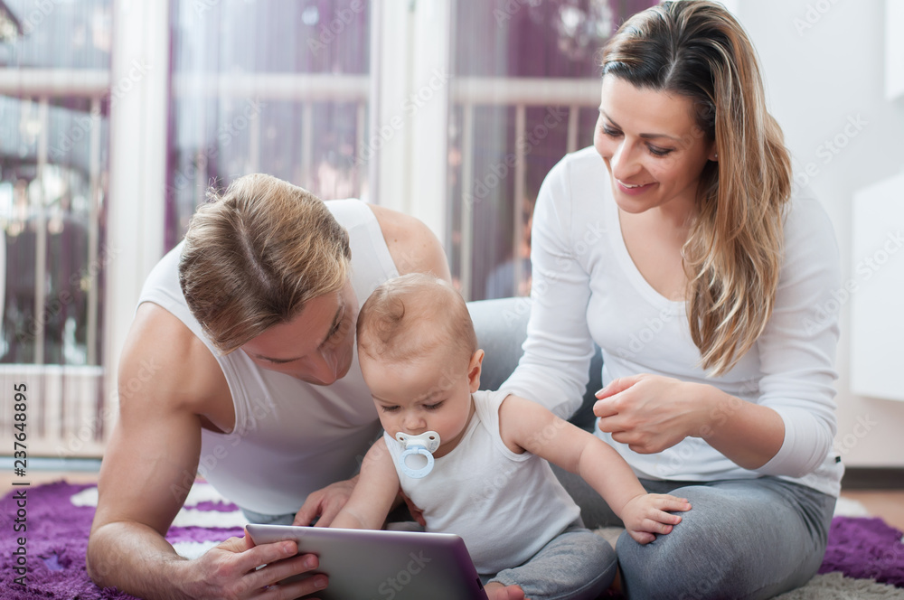 Happy parents laying down on the floor and playing on tablet with their baby boy Happy parents laying down on the floor and playing on tablet with their baby boy