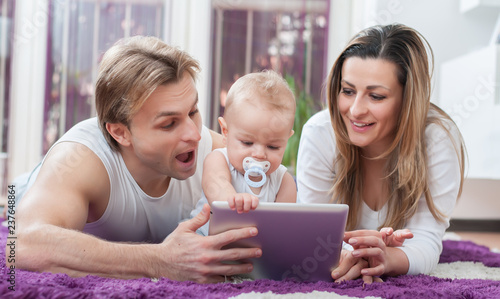 Happy parents laying down on the floor and playing on tablet with their baby boy