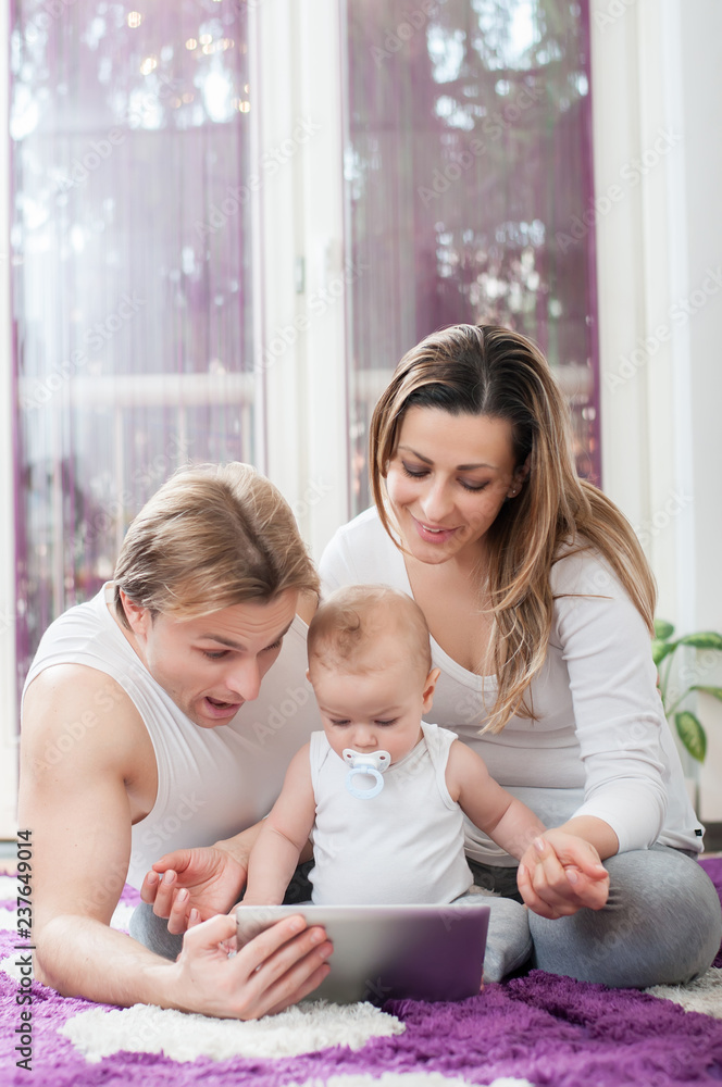 Happy parents laying down on the floor and playing on tablet with their baby boy Happy parents laying down on the floor and playing on tablet with their baby boy