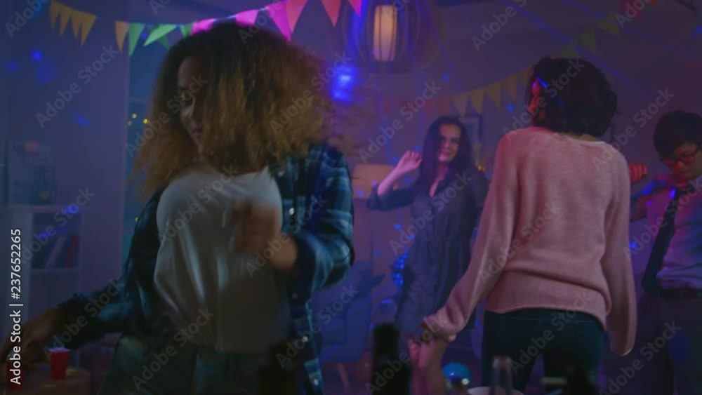 At the Wild House Party: Beautiful Black Girl Seductively Dances in Neon Lights. In the Background Other People Having Fun, Clubbing. In Slow Motion. At the Wild House Party: Beautiful Black Girl Seductively Dances in Neon Lights. In the Background Other People Having Fun, Clubbing. In Slow Motion.