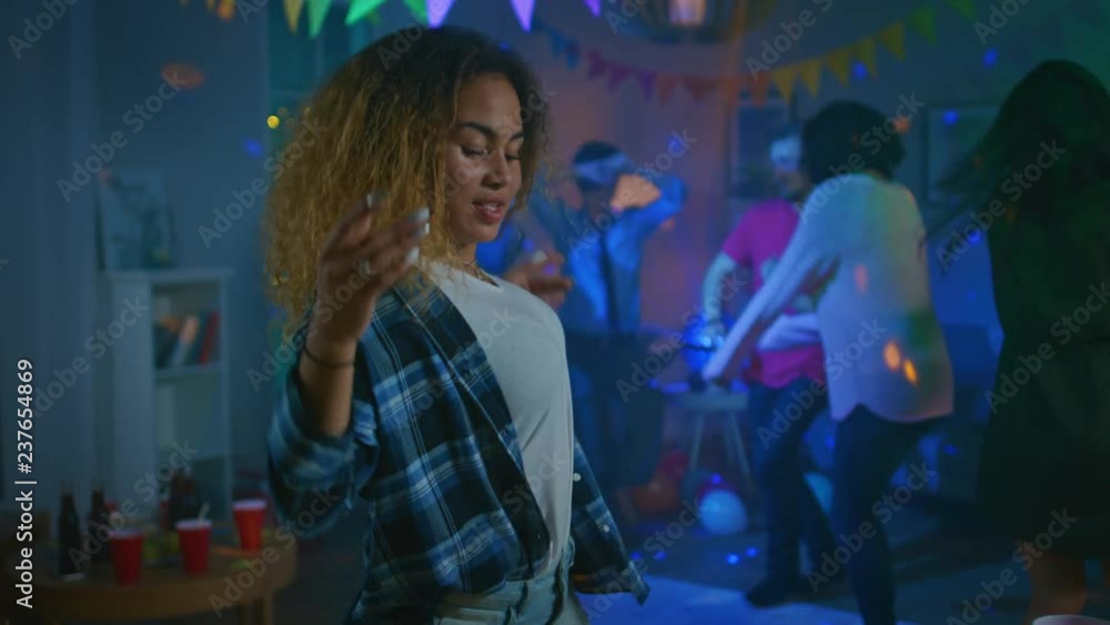 At the Wild House Party: Beautiful Black Girl Seductively Dances in Neon Lights. In the Background Other People Having Fun, Clubbing. At the Wild House Party: Beautiful Black Girl Seductively Dances in Neon Lights. In the Background Other People Having Fun, Clubbing.