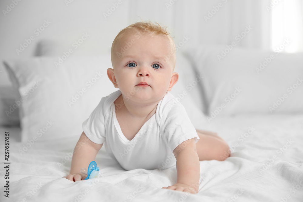 Cute baby with pacifier lying on bed at home