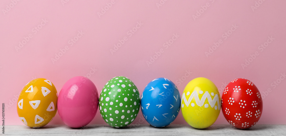 Obraz premium Decorated Easter eggs on table near color wall. Space for text
