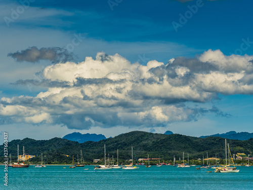 View over a busy harbour with lots of sailing boats, mountains in the background and huge fluffy clouds above