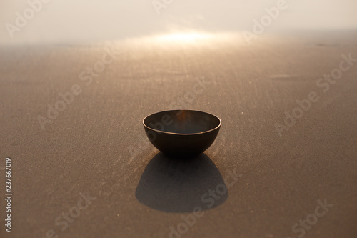 Tibetan singing bowl on the ocean on the sand. The background is blurred by sunlight. Place for inscription. Photo for advertising.