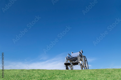 青空バックを背景に芝の上に置かれた無人の車イス。福祉、介護、病気、障害者、老後イメージ