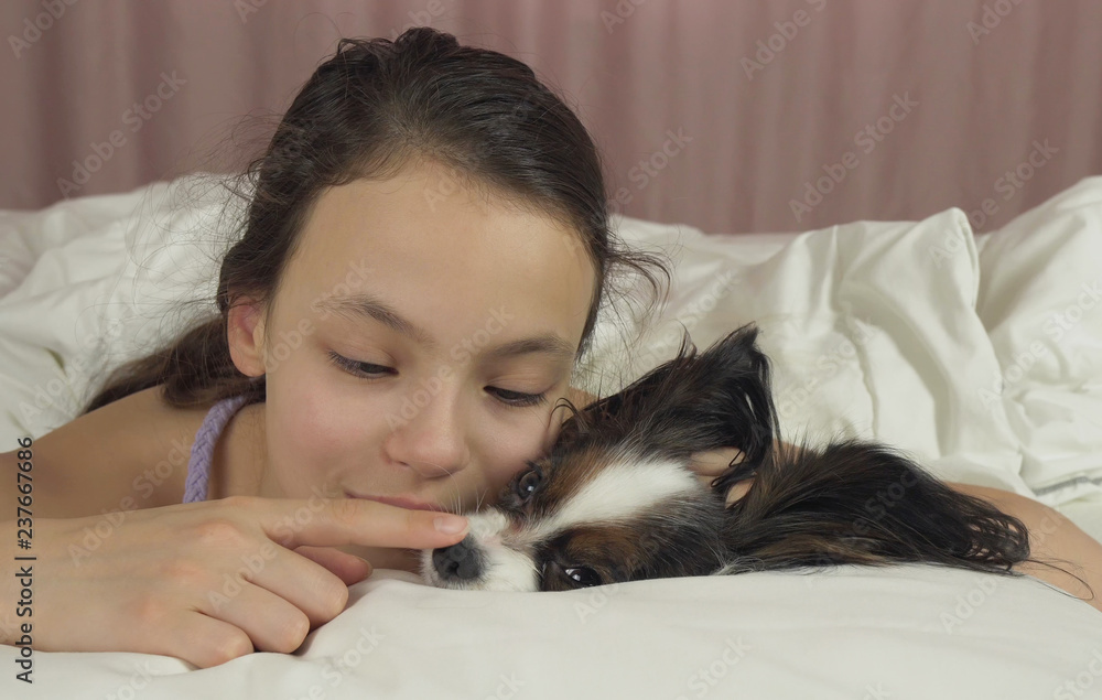 Happy teen girl kisses and plays with dog Papillon in bed Happy teen girl kisses and plays with dog Papillon in bed