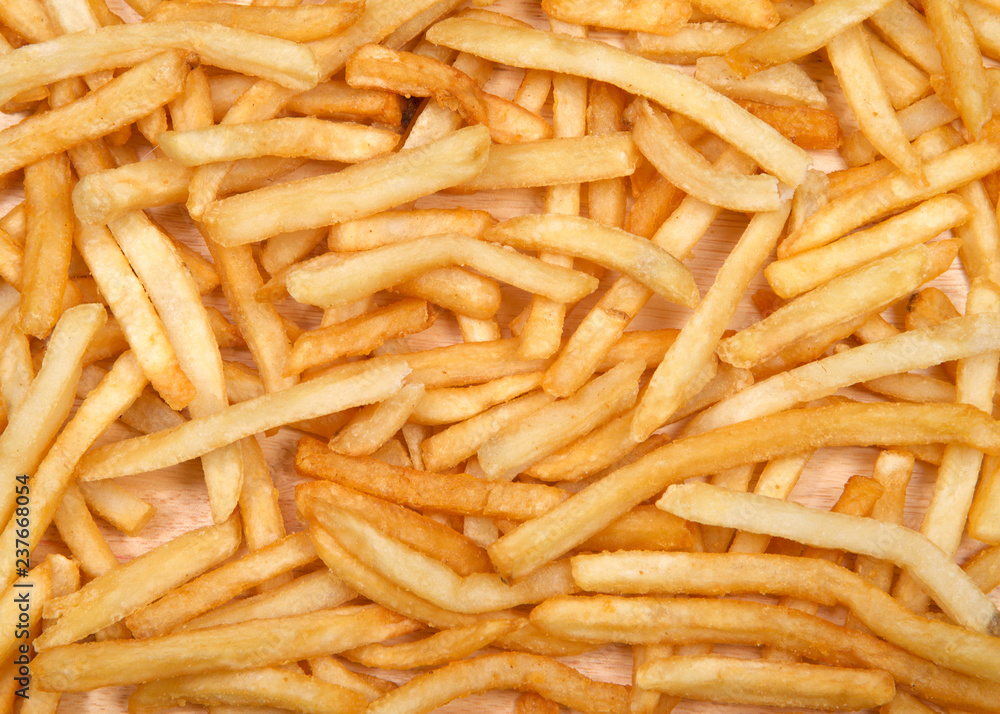Top view flat lay of many french fries on a light wood table. French fries have been popularized worldwide in large part by the large American fast food chains. Top view flat lay of many french fries on a light wood table. French fries have been popularized worldwide in large part by the large American fast food chains.