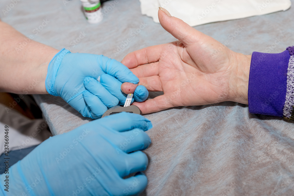 Doctor taking sample of diabetic patient's blood using lancet pen, closeup.Diabetes test on blood sample of old woman in examination at gynecologist office.Checking the glucose level with a glucometer Doctor taking sample of diabetic patient's blood using lancet pen, closeup.Diabetes test on blood sample of old woman in examination at gynecologist office.Checking the glucose level with a glucometer