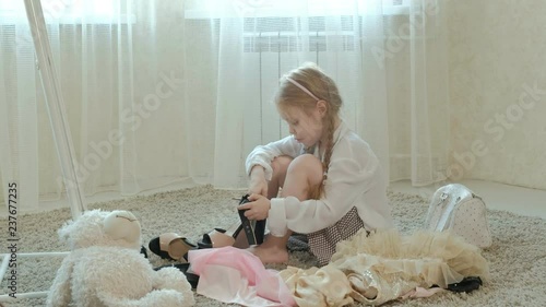 cheerful girl with pigtails in a pink skirt tries on adult mother's clothes, dresses, high heels and dances in front of a mirror with a bag, mothers wardrobe