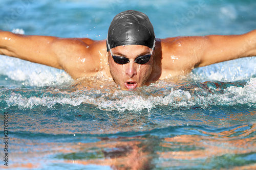 Swimmer. Man swimming butterfly strokes in pool competition. Competitive male sport athlete swimmer wearing swimming goggles and cap. Young caucasian fitness model face portrait. © Maridav