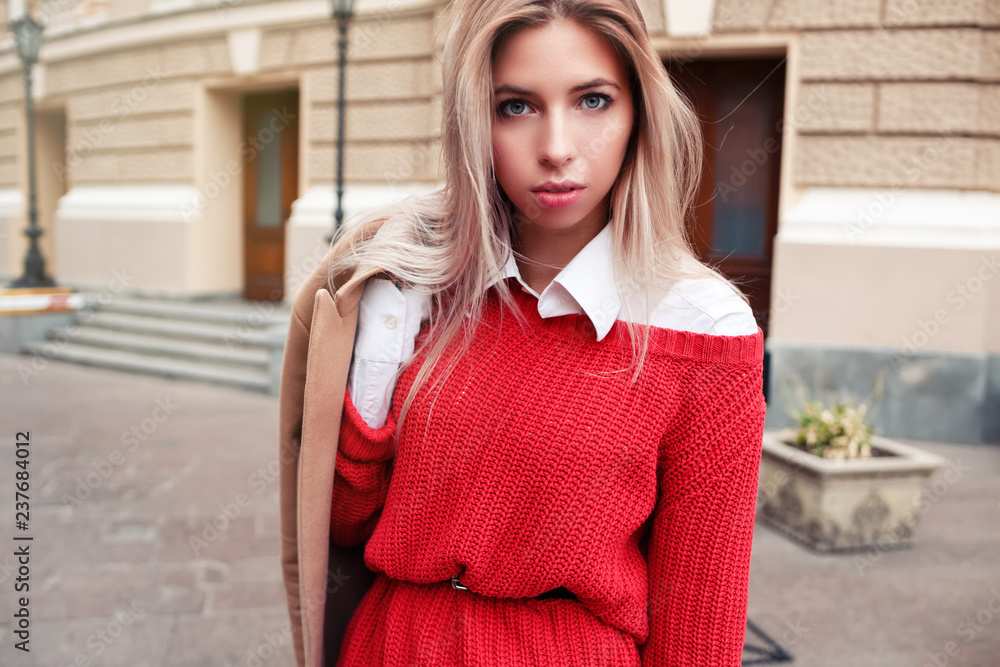Beautiful blond young woman wearing dress and beige jacket and walking on the street.Street portrait of a young beautiful elegant woman.Lady wearing stylish spring clothes Beautiful blond young woman wearing dress and beige jacket and walking on the street.Street portrait of a young beautiful elegant woman.Lady wearing stylish spring clothes
