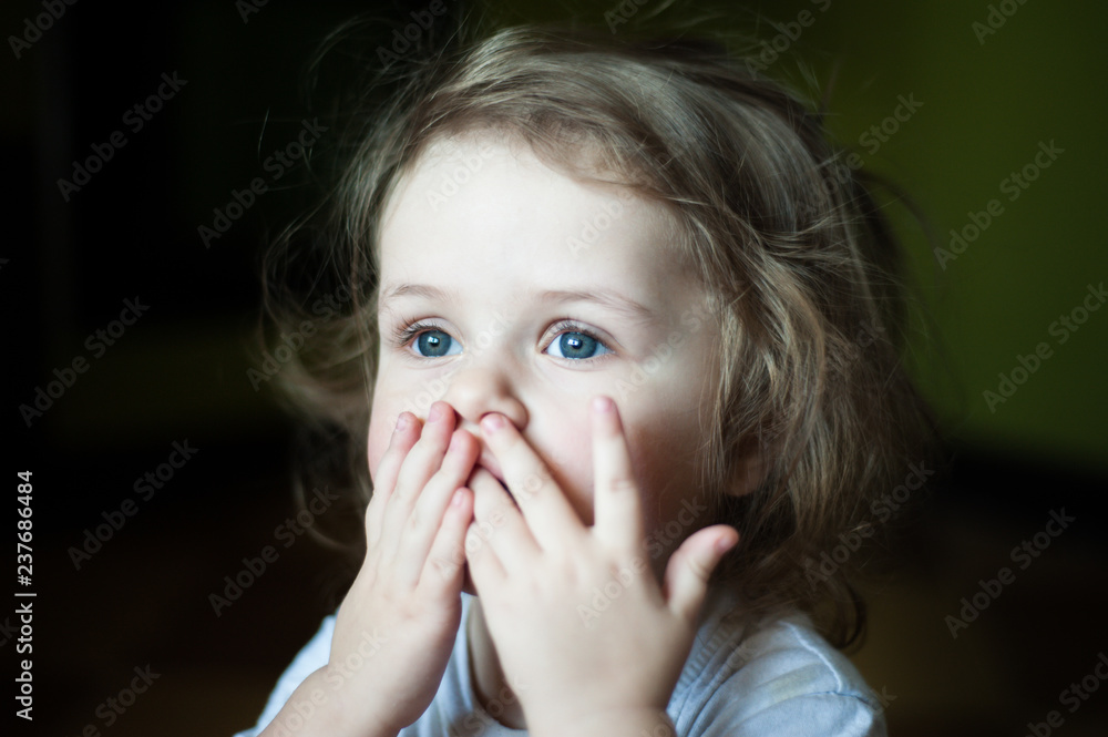 Closeup portrait of a child. She closed her mouth with both hands. Fears. Shaggy girl. Emotional concept Closeup portrait of a child. She closed her mouth with both hands. Fears. Shaggy girl. Emotional concept