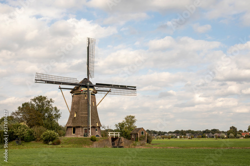 Traditional dutch windmill in the countryside in the Netherlands surrounded by pasture under a blue cloudy sky. 