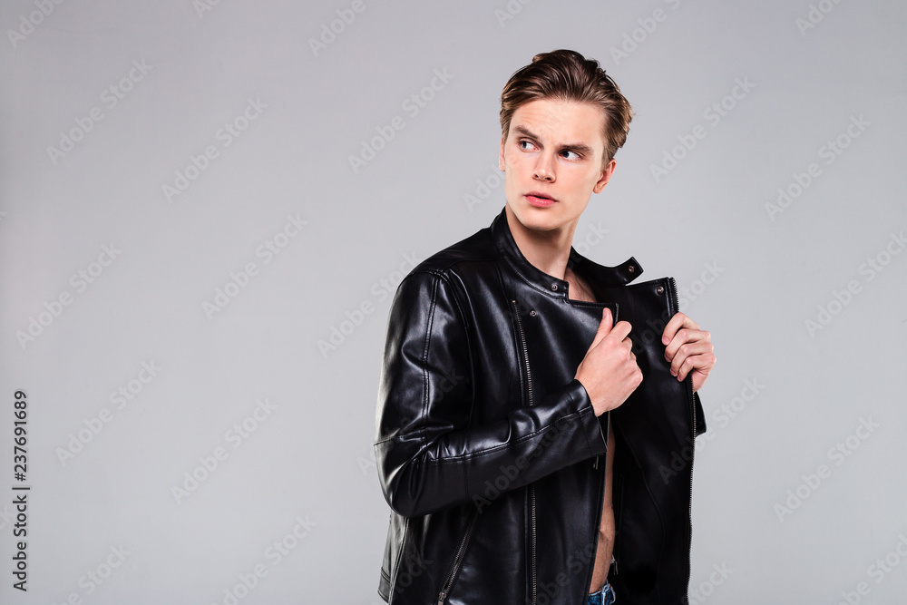 Take a look at this handsome! Handsome shirtless young man in leather jacket looking away while standing against grey background Take a look at this handsome! Handsome shirtless young man in leather jacket looking away while standing against grey background