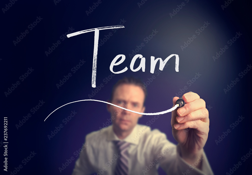 A businessman writing a Team concept with a white pen on a clear screen. A businessman writing a Team concept with a white pen on a clear screen.