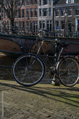 Usual black bike near the canal in the center of Amsterdam in the sunny autumn day
