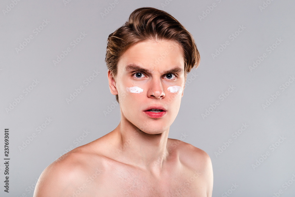Newer forget about moisturizer. Portrait of handsome shirtless young man with cream on his face and looking at camera while standing against grey background Newer forget about moisturizer. Portrait of handsome shirtless young man with cream on his face and looking at camera while standing against grey background