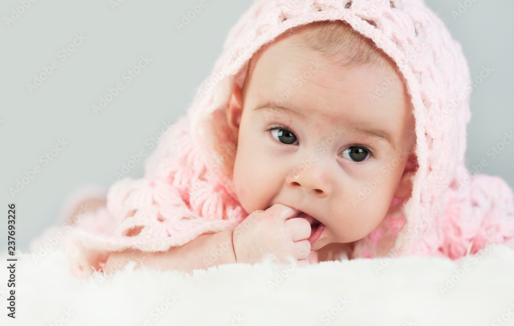 Portrait of a crawling beautiful bright baby in the hood on the bed in his room. Suck a hand. Portrait of a crawling beautiful bright baby in the hood on the bed in his room. Suck a hand.