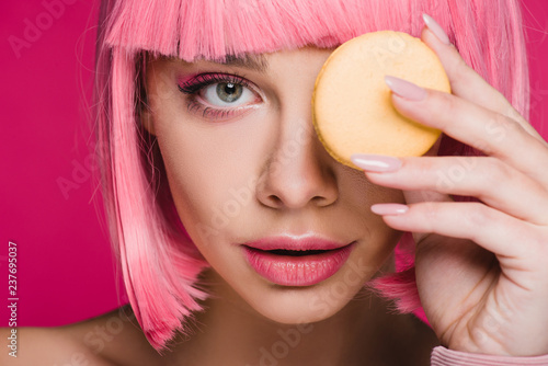 attractive girl in pink wig posing with yellow macaron isolated on pink