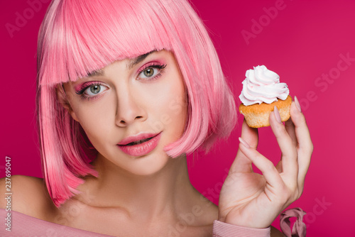 beautiful girl in pink wig holding delicious cupcake isolated on pink