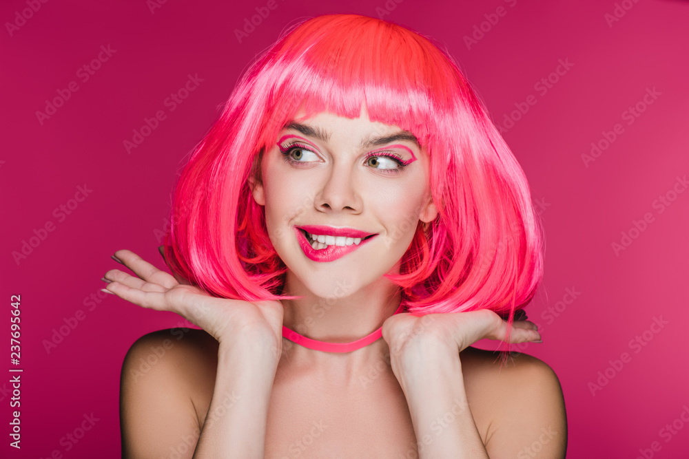 beautiful girl biting lip and posing in neon pink wig, isolated on pink beautiful girl biting lip and posing in neon pink wig, isolated on pink