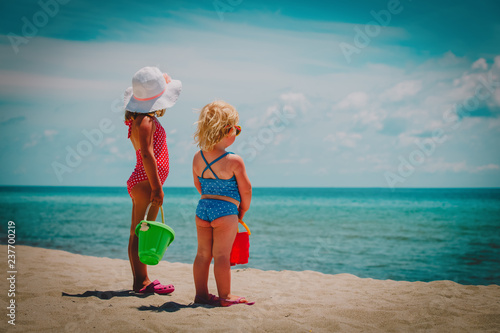 little girls play with sand on summer beach