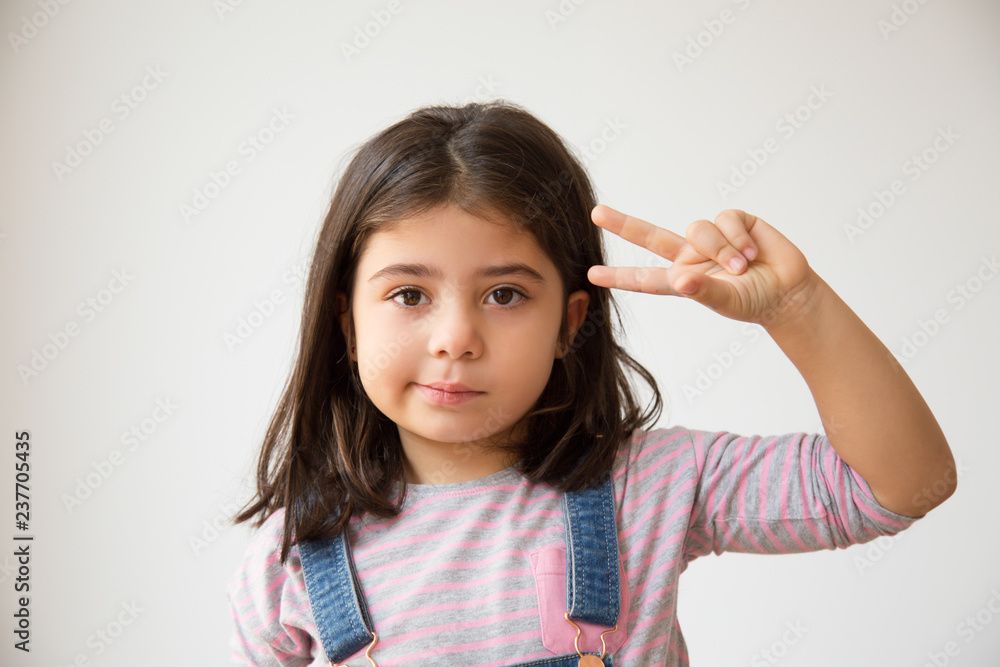 Adorable Latin child showing two fingers. Little confused girl with peace symbol looking at camera. Isolated on white. Gesturing concept Adorable Latin child showing two fingers. Little confused girl with peace symbol looking at camera. Isolated on white. Gesturing concept